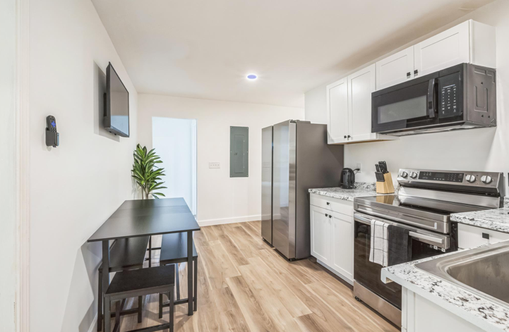 PadSplit kitchen in Atlanta with stainless steel refrigerator and range, white shaker cabinets, granite counters, wall mounted TV and a compact dining table