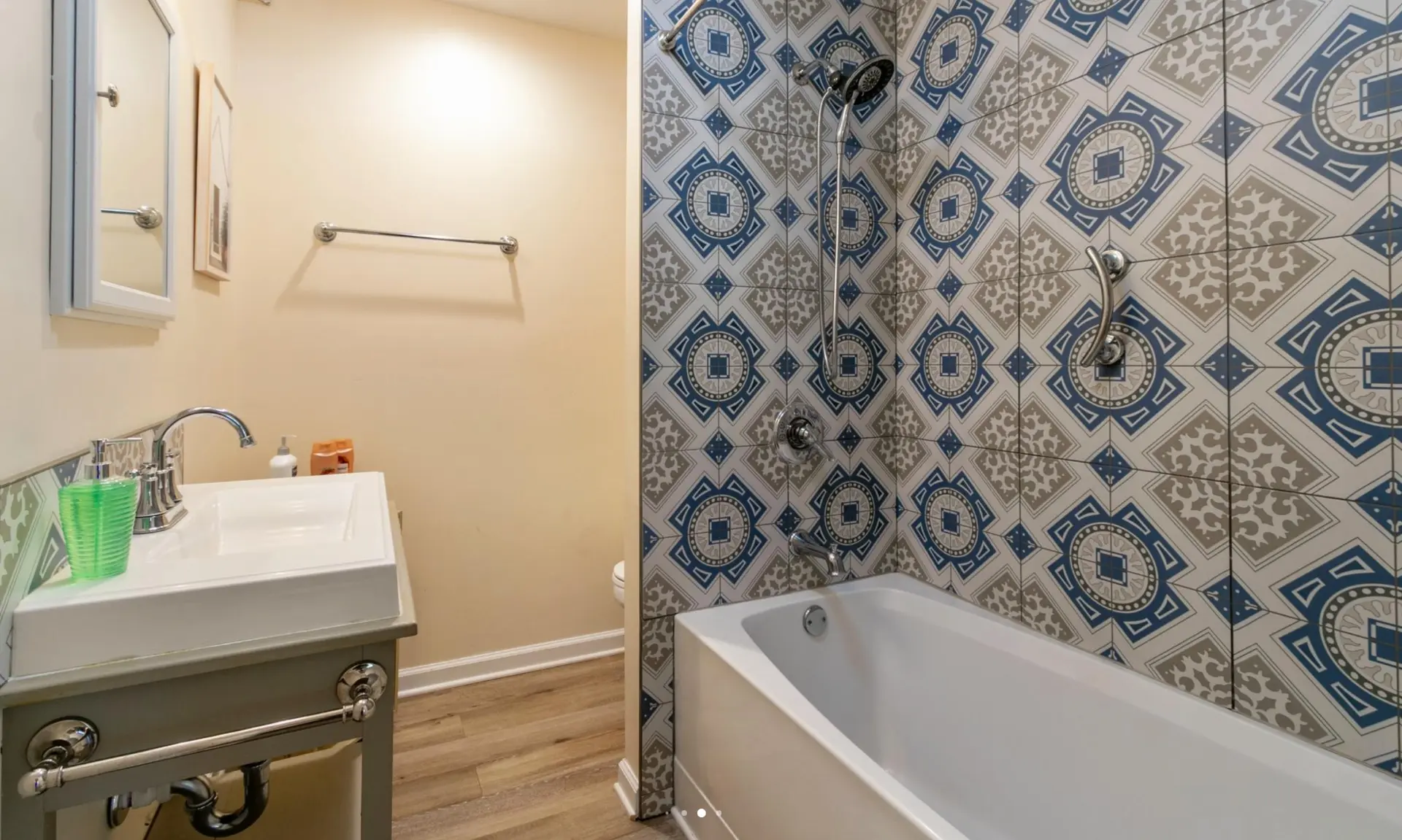 Cleaned Atlanta rental bathroom with a white vanity sink, mirrored cabinet and patterned blue tile tub and shower surround