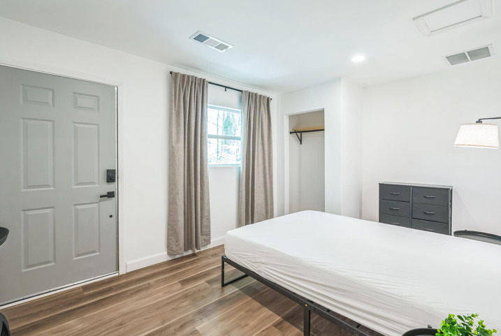 Bright PadSplit bedroom in Atlanta with a made platform bed, gray dresser, wall sconce and curtained window