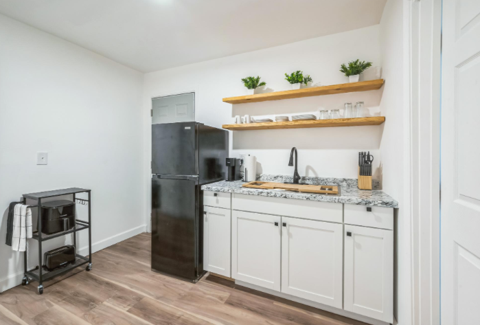 Private kitchenette in an Atlanta PadSplit room with a black refrigerator, granite counter sink, open wood shelving and coffee station